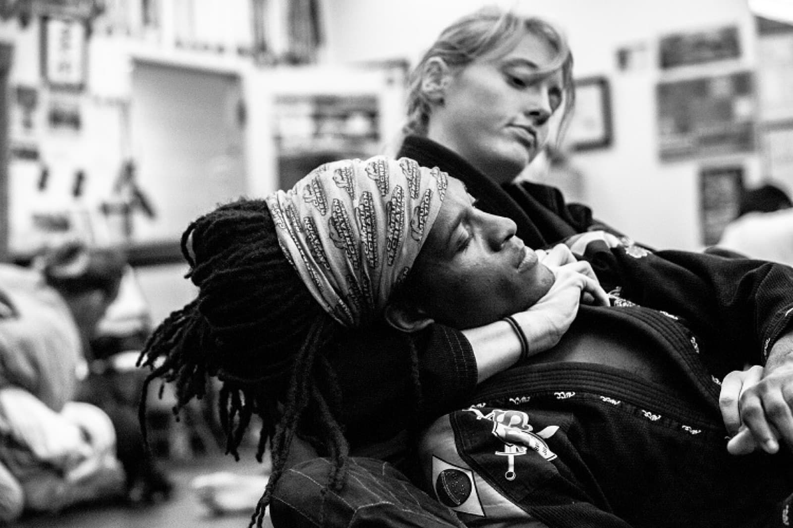 Two women training jiu-jitsu, one controlling her partner from behind