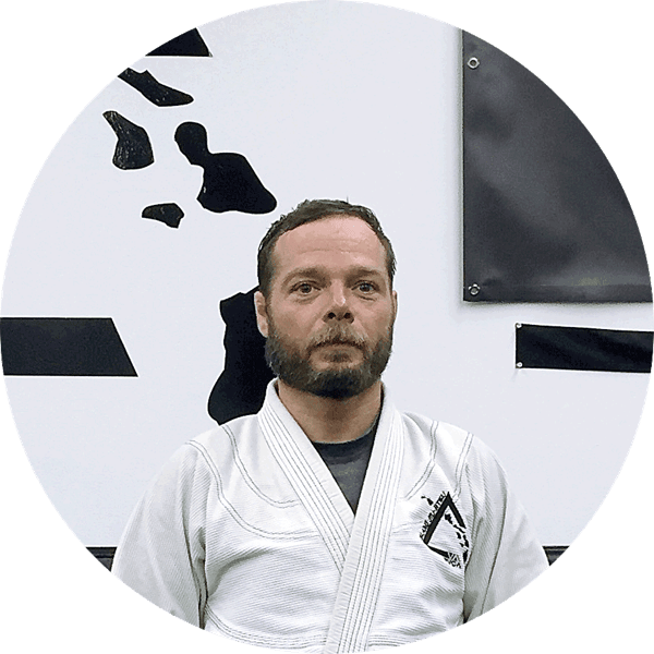 Chris Ledman in a white gi in front of the Island Jiu-Jitsu logo wall
