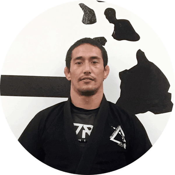 Kawena Mitchell in a black gi in front of the Island Jiu-Jitsu logo wall