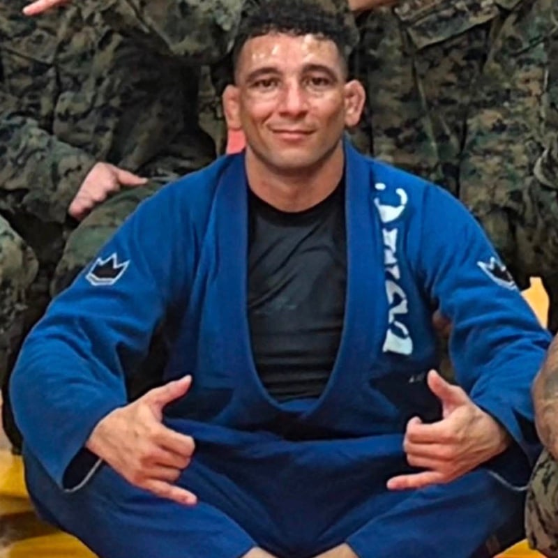 Professor Murvil “Rusty” Lipsey in a blue gi, seated on the mats throwing double shakas