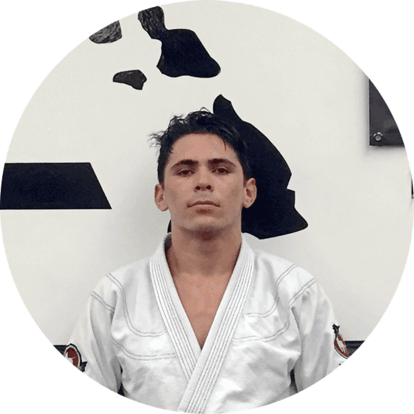 Nick Alcoran in a white gi in front of the Island Jiu-Jitsu logo wall