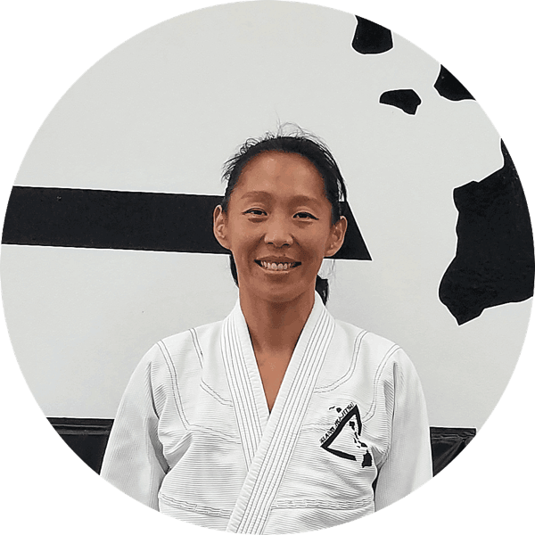 Tammy Chang smiling in a white gi in front of the Island Jiu-Jitsu logo wall