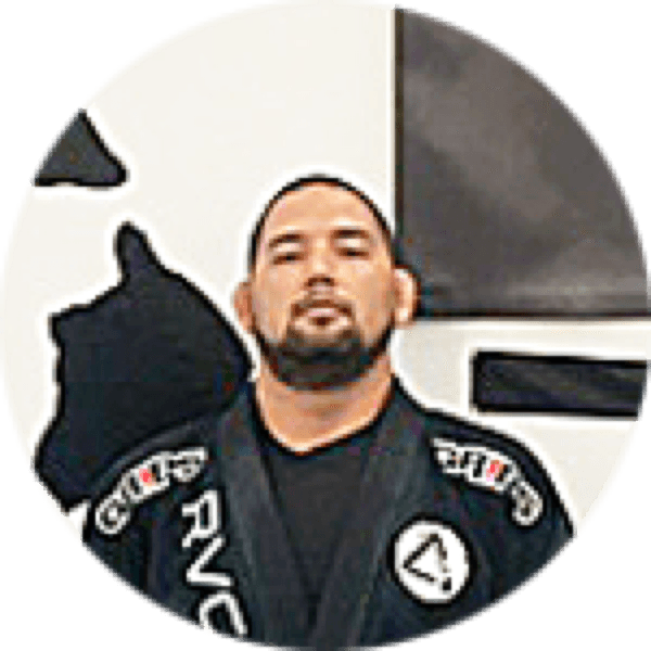 Taylor Kuhia in a black gi in front of the Island Jiu-Jitsu logo wall
