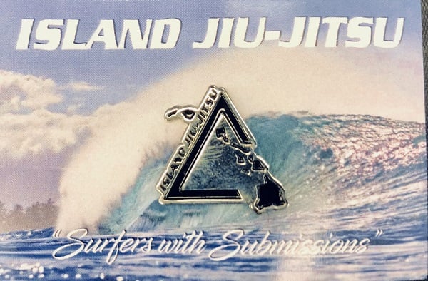 Silver and black IJJ triangle logo lapel pin on a backing card printed with a breaking wave and the words Surfers with Submissions