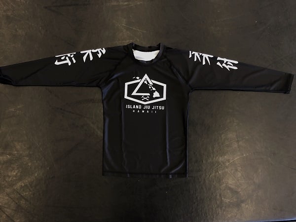 Black long-sleeve IJJ rash guard laid flat, with the white hexagon Island Jiu Jitsu Hawaii logo on the chest and jiu-jitsu kanji down each sleeve