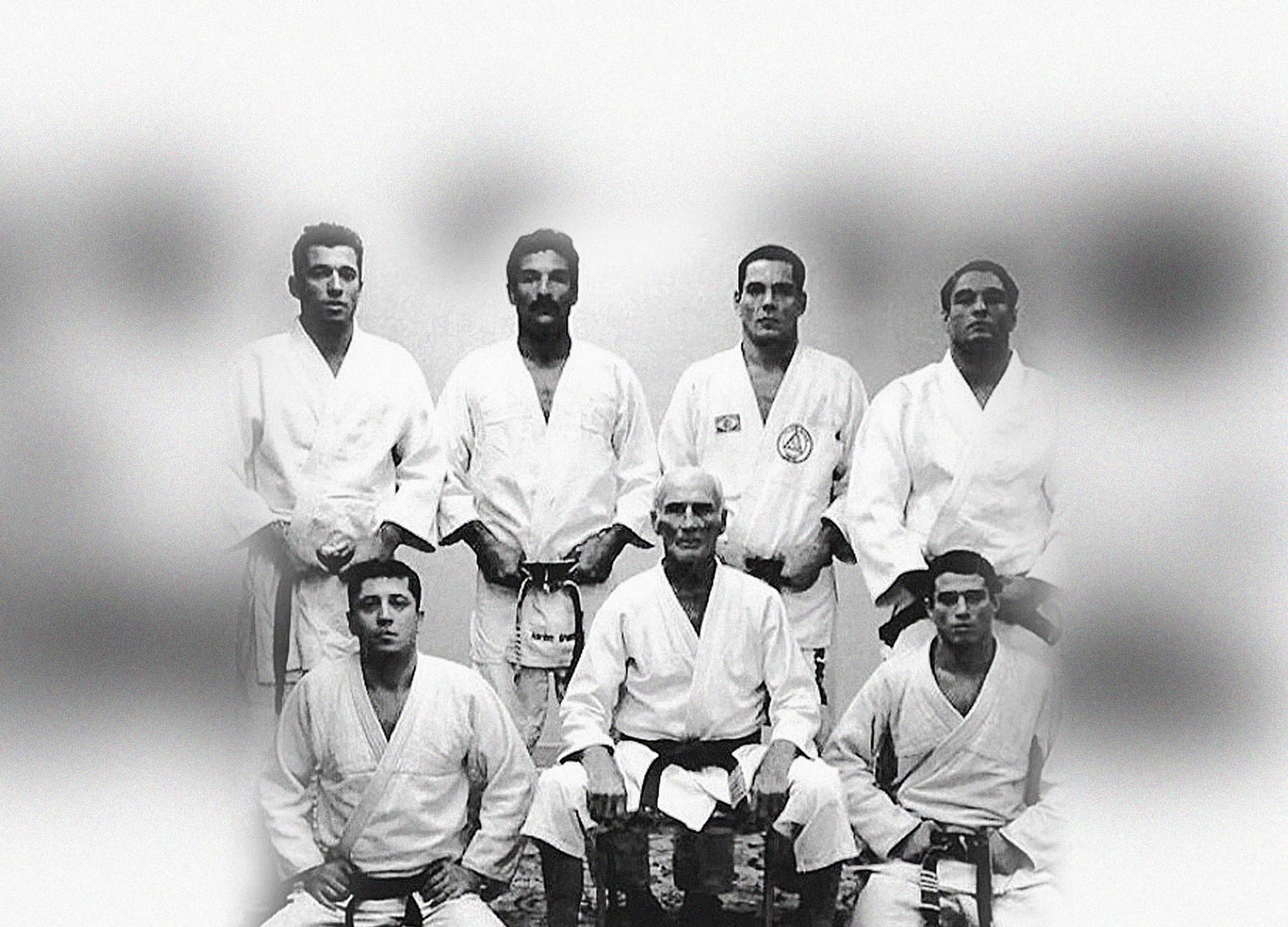 Black-and-white portrait of Helio Gracie seated, surrounded by members of the Gracie family in their gis