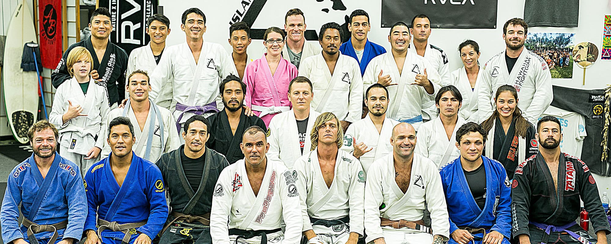 The Island Jiu-Jitsu team in their gis, posing together in front of the triangle logo on the dojo wall